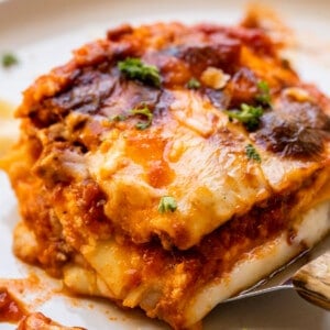 putting a piece of lasagna on a white plate with a spatula.