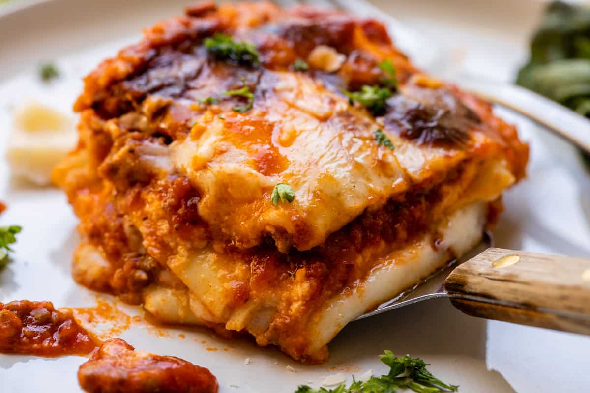 close up shot of a square of homemade lasagna on a white plate.