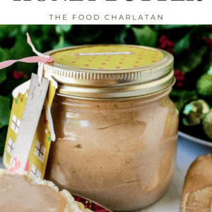 A jar of cinnamon butter with a yellow checkered lid sits on a table next to a biscuit spread with the sweet butter. A small house-shaped gift tag is attached to the jar.