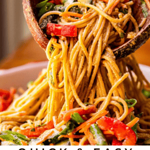 sesame noodles recipe being lifted from a white bowl with wooden spoons.
