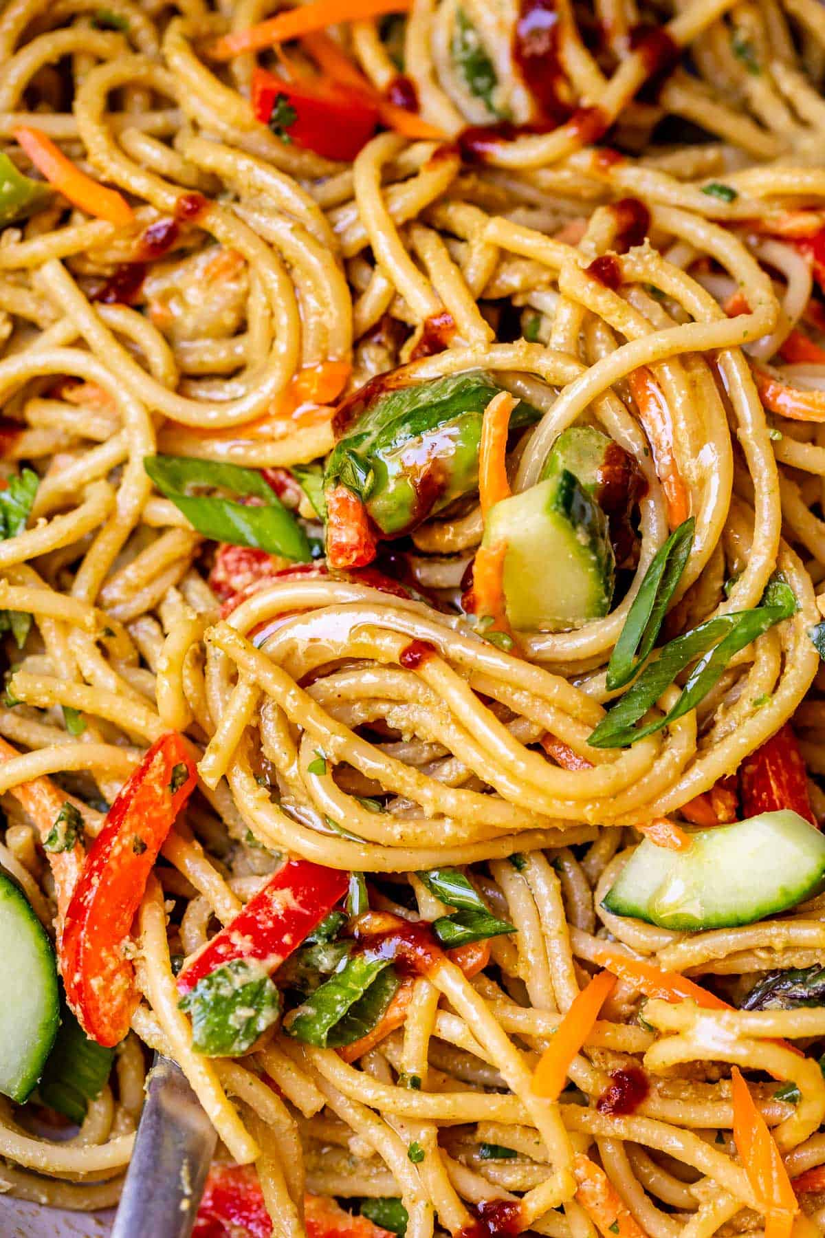 close up of swirled, cold noodles with sesame sauce and vegetables mixed in.