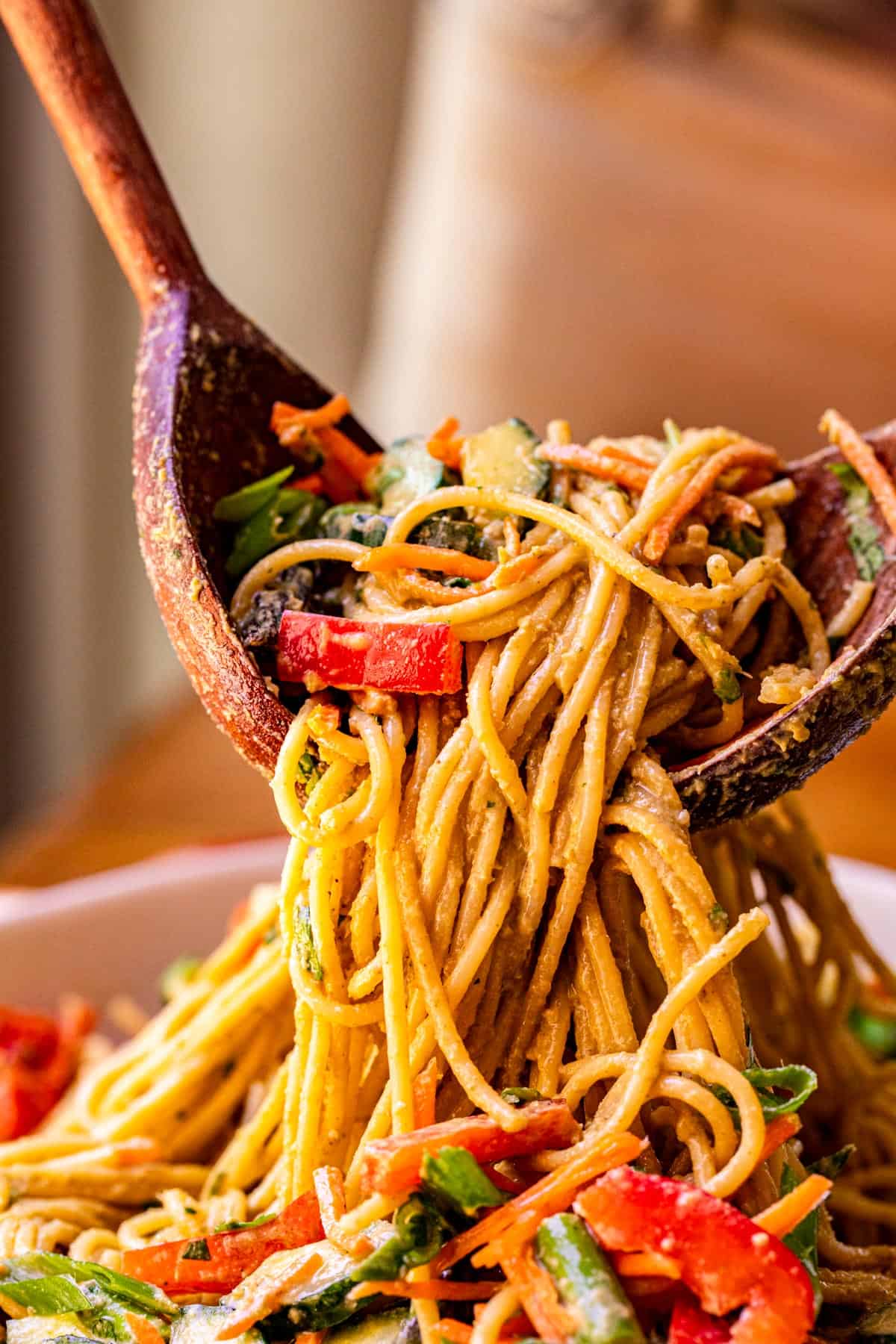 sesame peanut noodles being lifted up by two wooden salad spoons to serve.