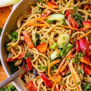 individual ceramic bowl filled to the top with sesame noodle recipe and vegetables.
