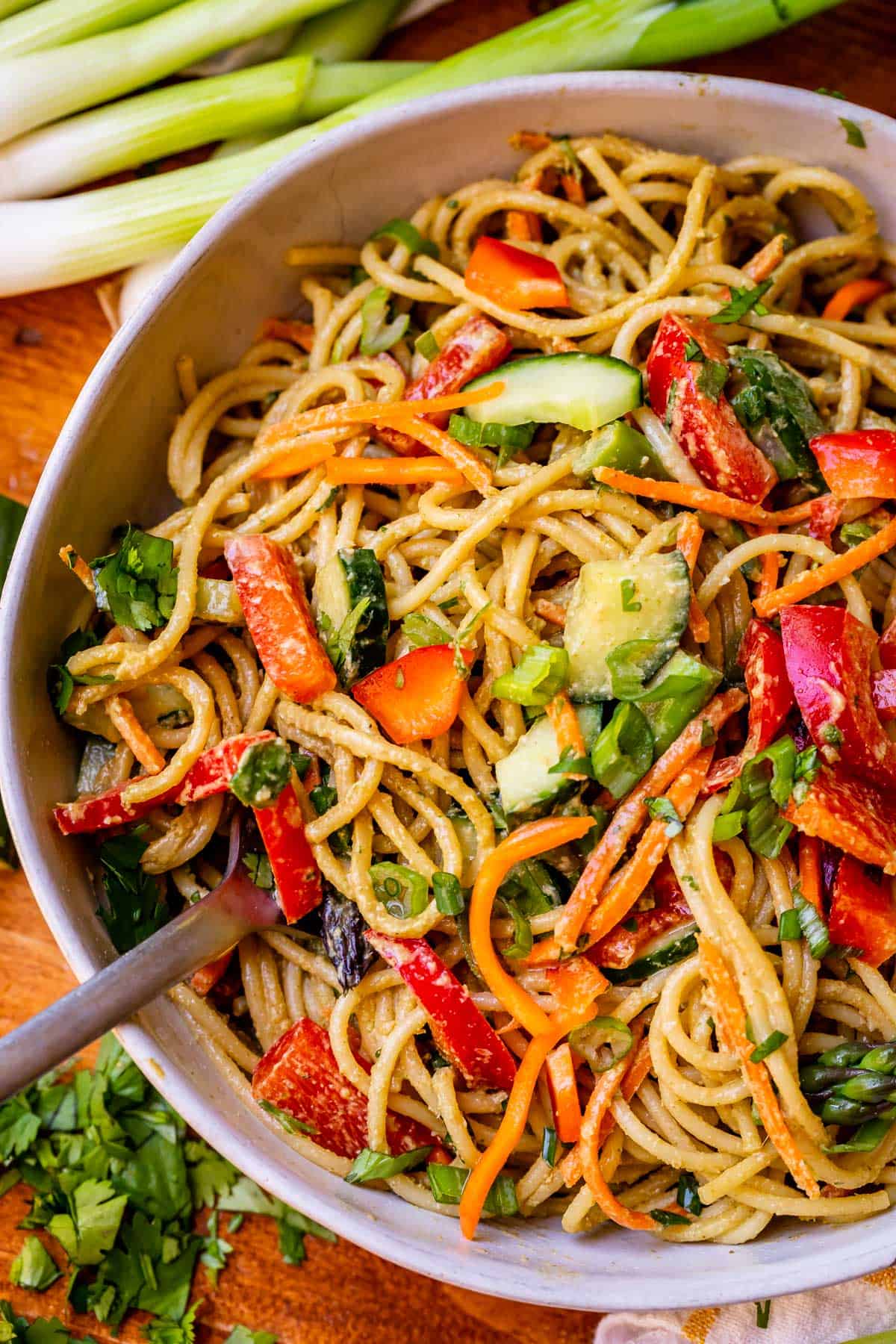 individual ceramic bowl filled to the top with sesame noodle recipe and vegetables.