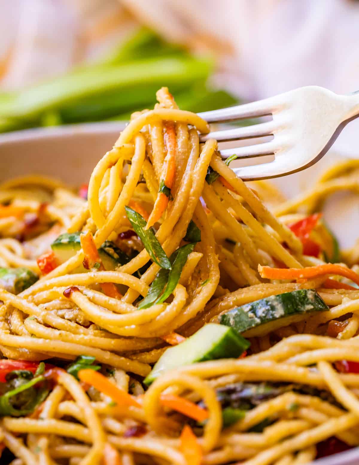 close up of thin spaghetti noodles covered in sesame sauce being lifted up by a fork.