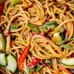 sesame peanut noodles swirled with vegetables in a large ceramic bowl.
