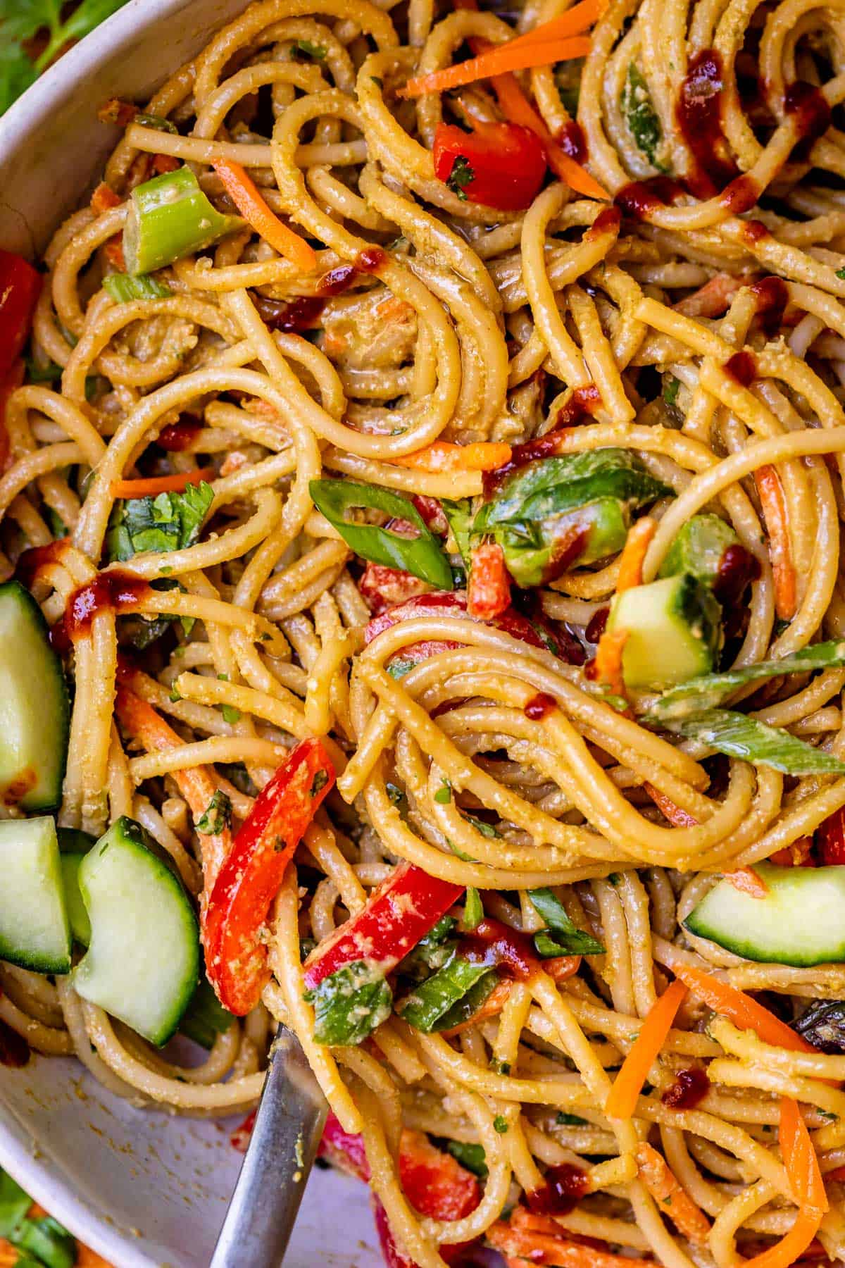 sesame peanut noodles swirled with vegetables in a large ceramic bowl.