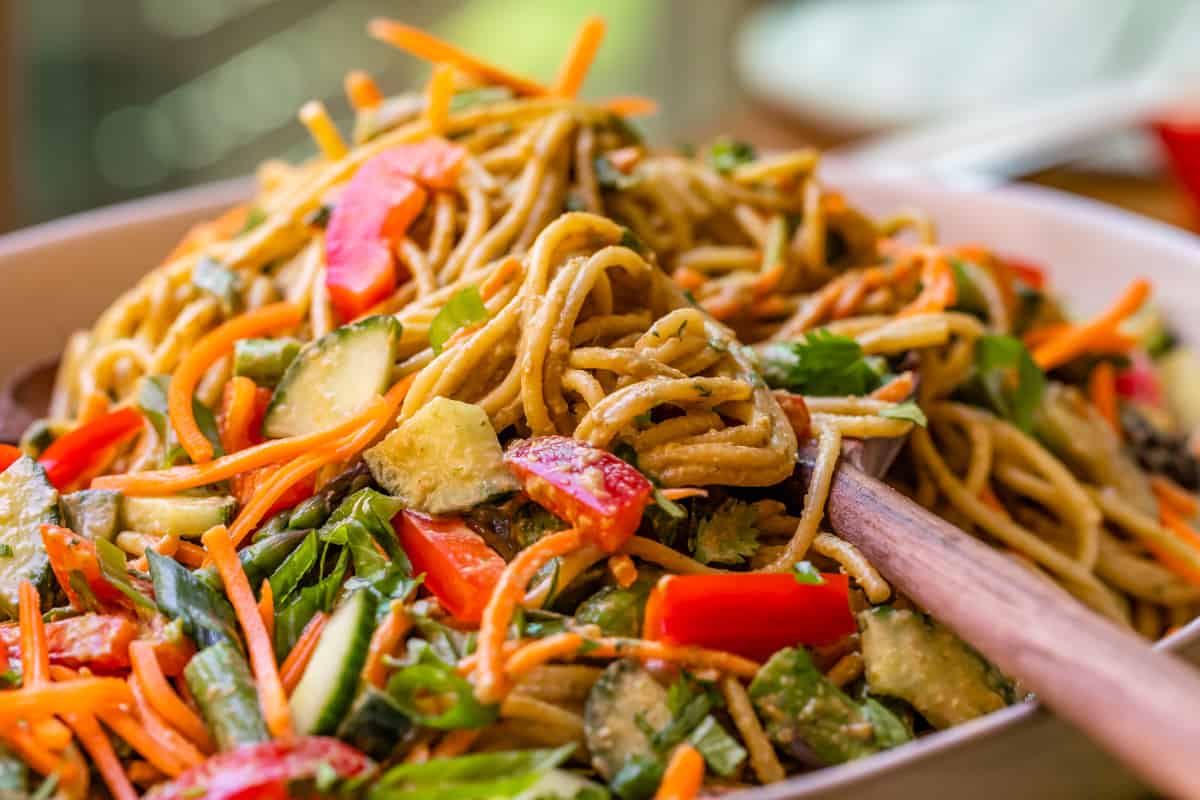 side view of cold noodles and vegetables topped in sesame sauce heaping in a bowl.