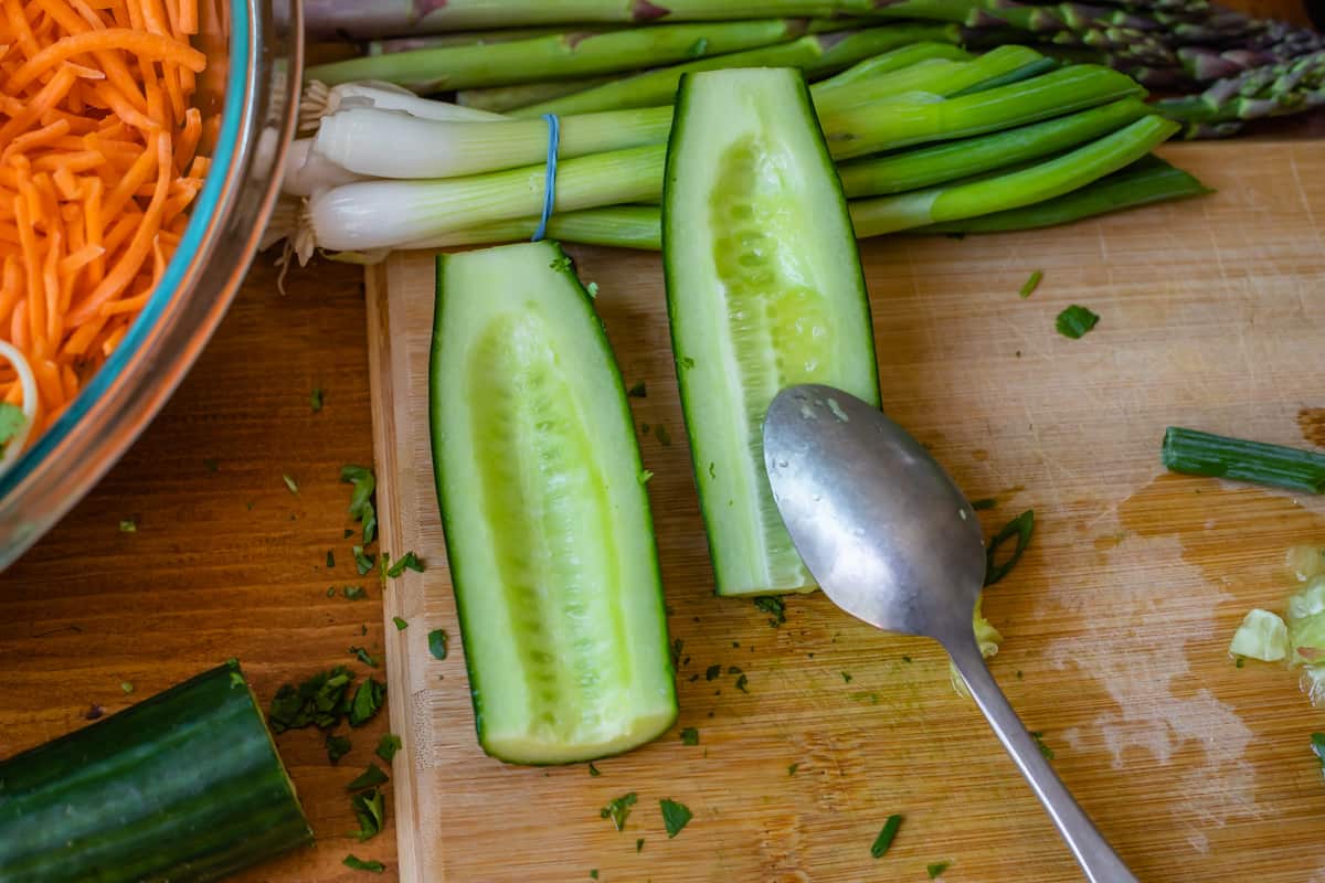 the seeds of a cucumber being scraped out by a spoon to add to sesame noodles.