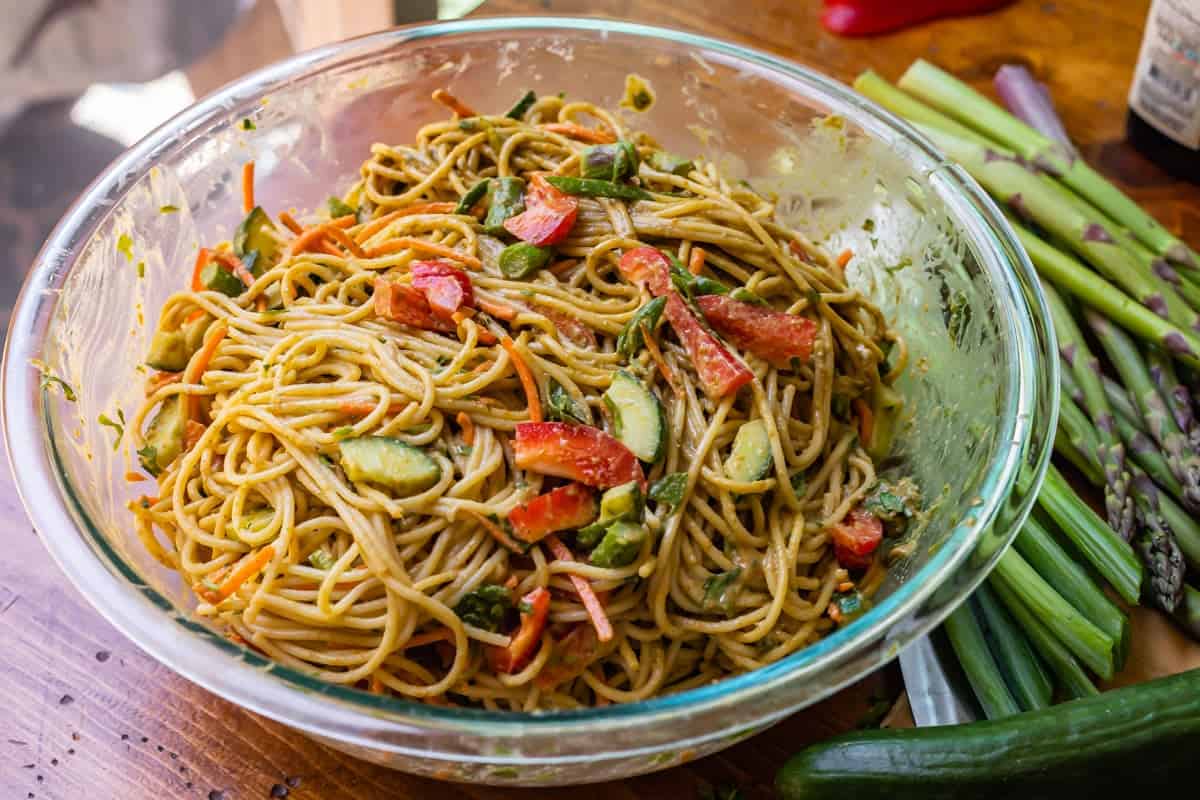 noodles mixed with the sesame sauce and vegetables in a glass bowl.