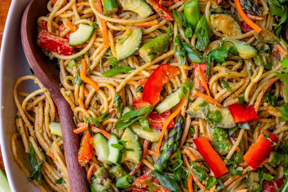 close up of cold sesame noodles with red pepper, cucumber, and asparagus in bowl.