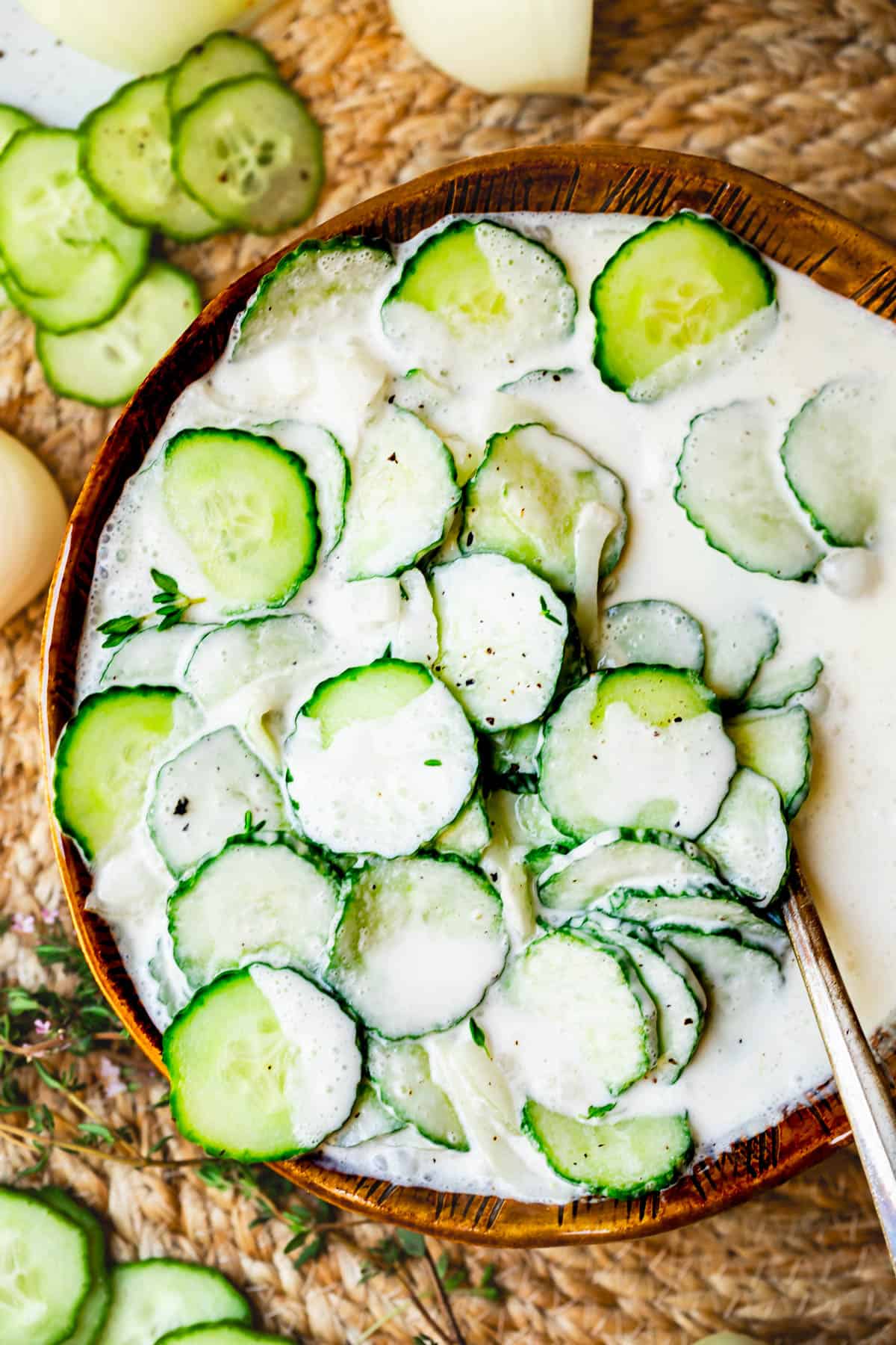 creamy cucumber salad in a brown clay bowl with onions and thyme, on a woven placemat.