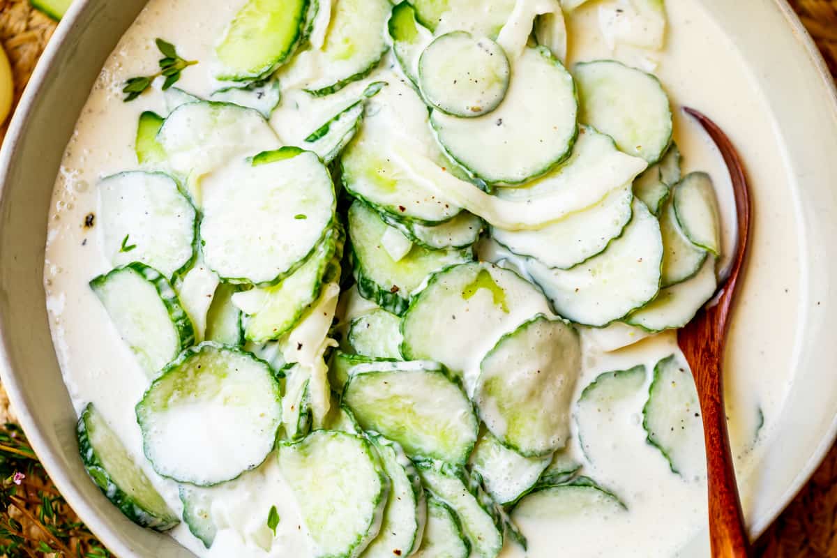 horizontal photo of creamy cucumbers in a white bowl with a wooden spoon.