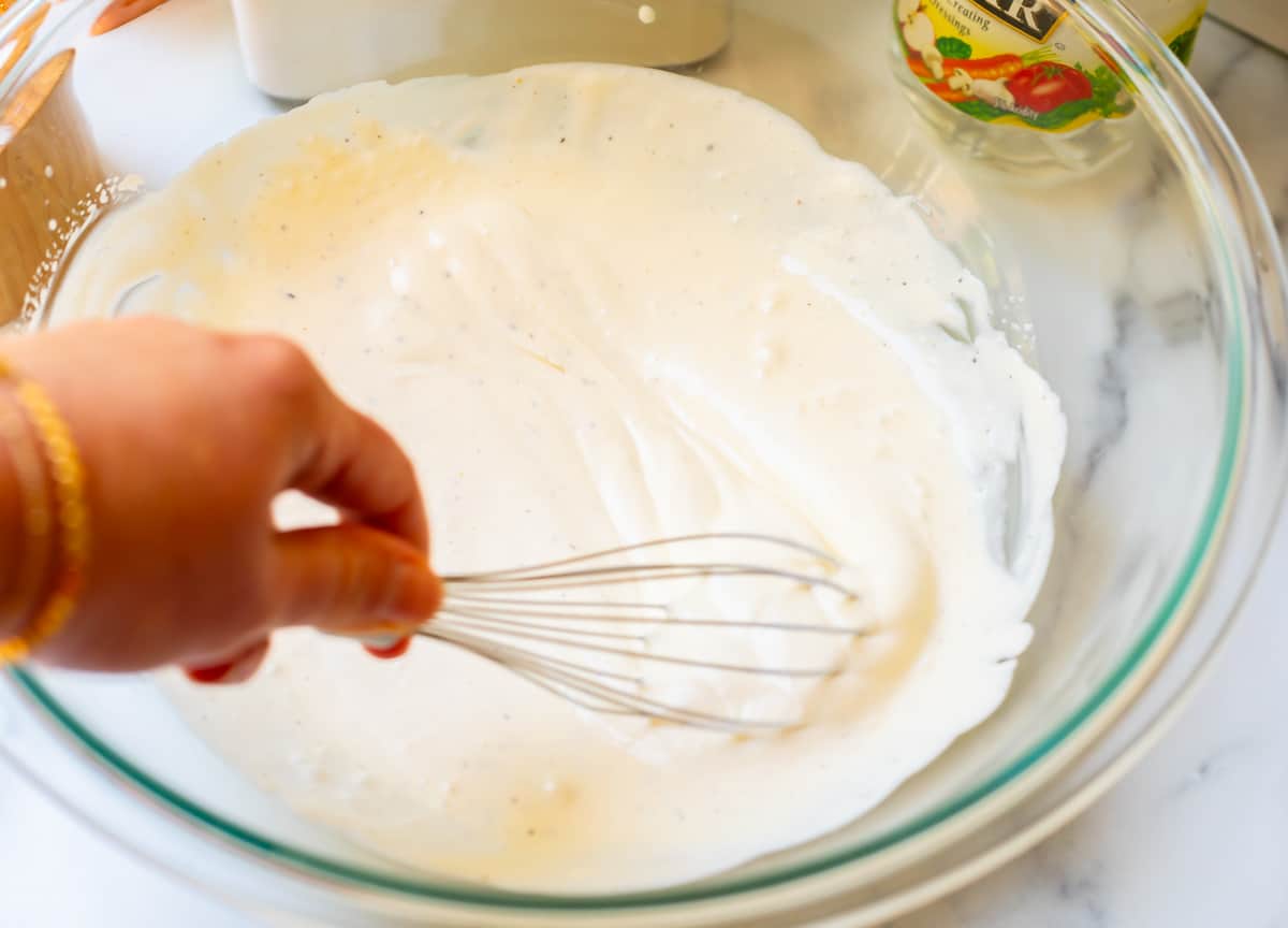 Stirring creamy sauce with whisk in large glass bowl.