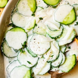 creamy cucumber salad with onions and thyme in a white bowl with wooden spoon.