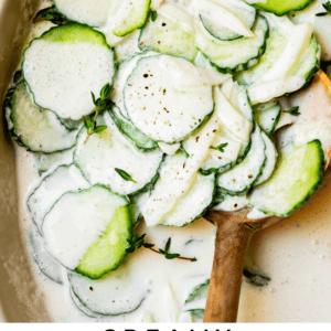bowl of sliced cucumbers in a creamy dressing with wooden spoon.