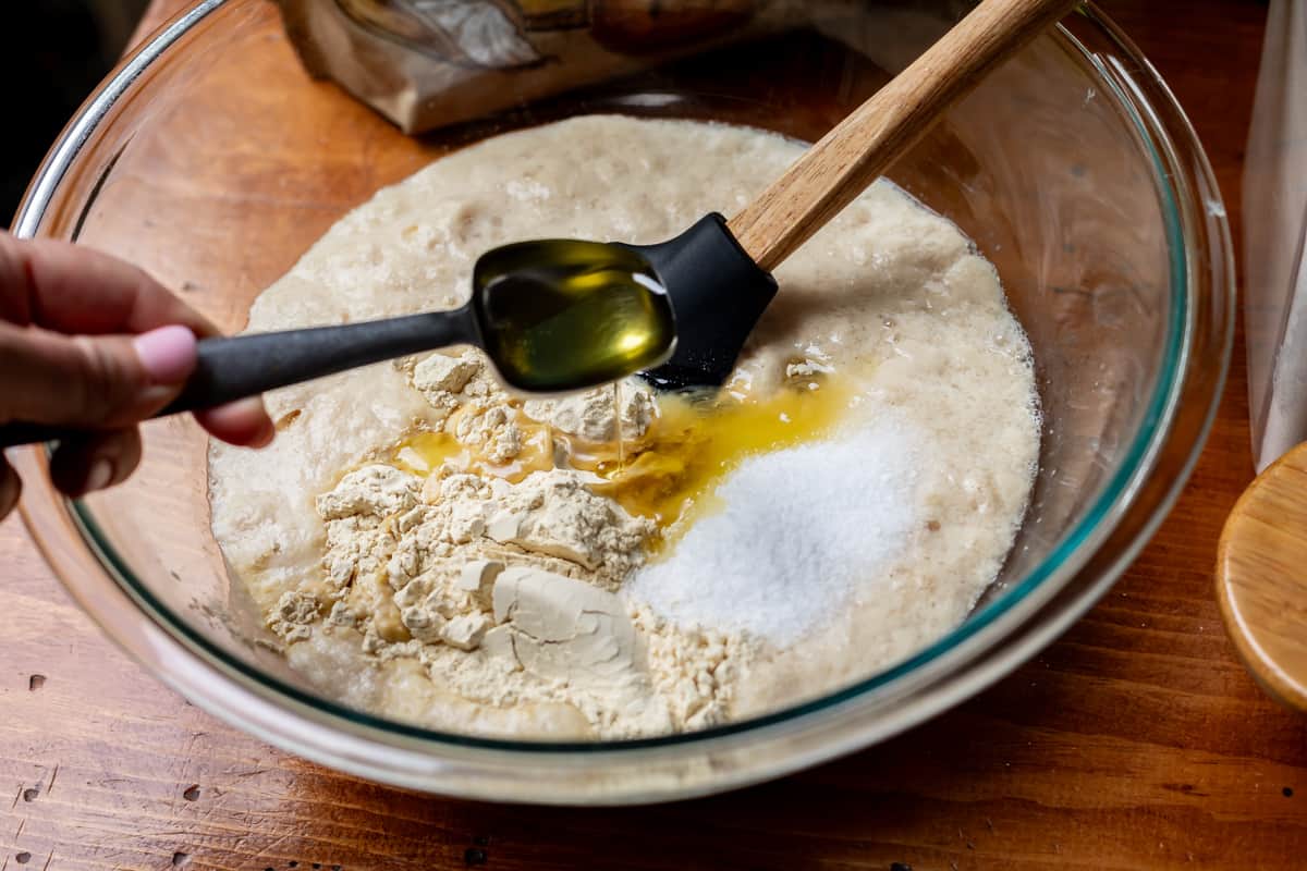 glass bowl with yeast mixture adding oil, sugar, and vital wheat gluten for extra rise.