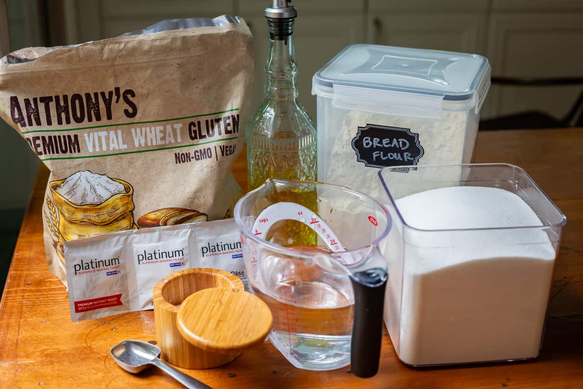 ingredients for homemade bread laid out on a table: flour, oil, sugar, water, yeast, etc.