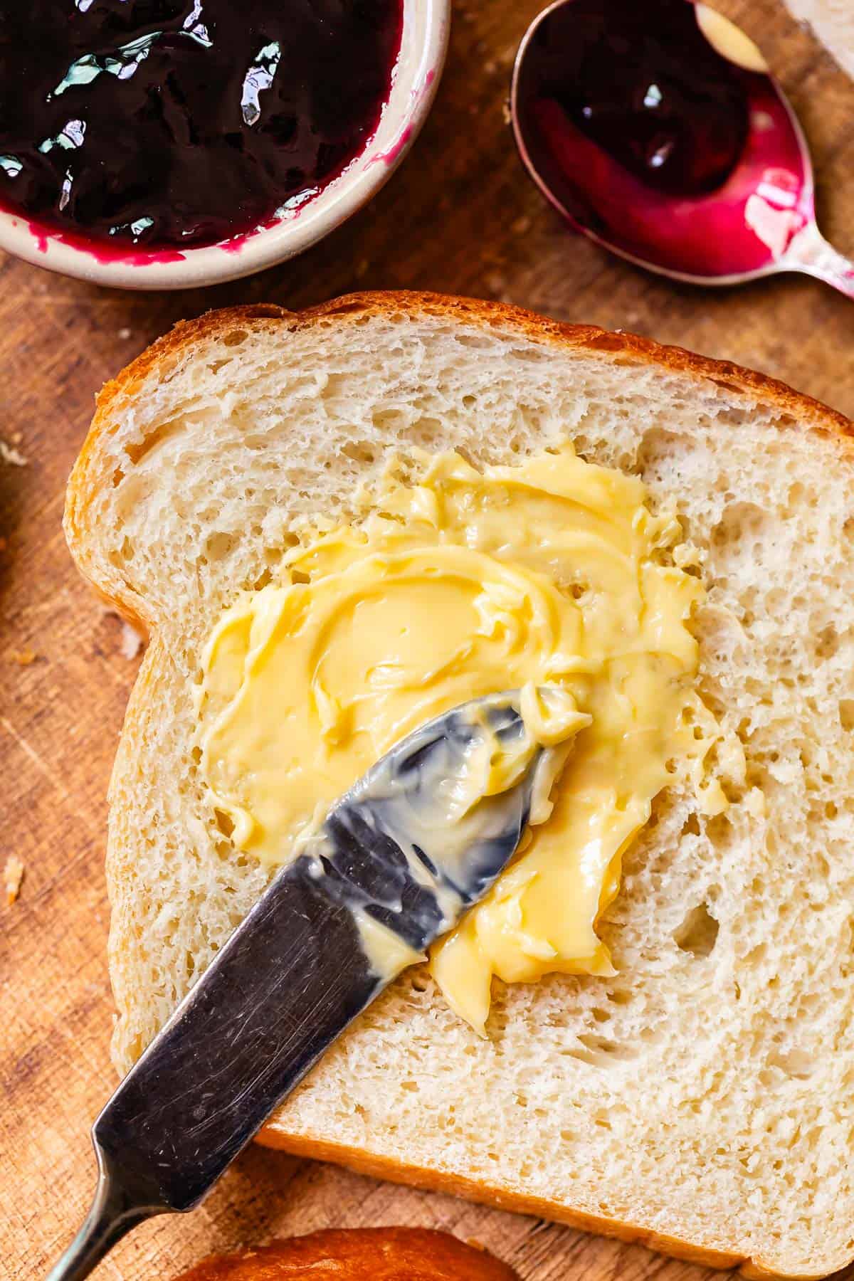 a butter knife spreading softened butter on a single piece of homemade white bread .