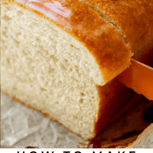 a bread knife carefully cutting a thick slice from a whole loaf of homemade white bread.