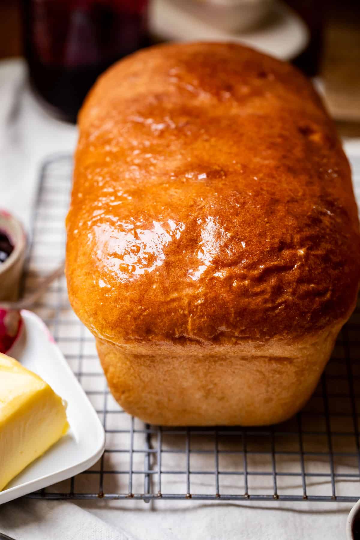 a whole loaf of uncut white bread out of the pan sitting on a cooling rack.