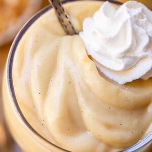 single glass cup of creamy vanilla pudding with a spoon and a dollop of whipped cream.