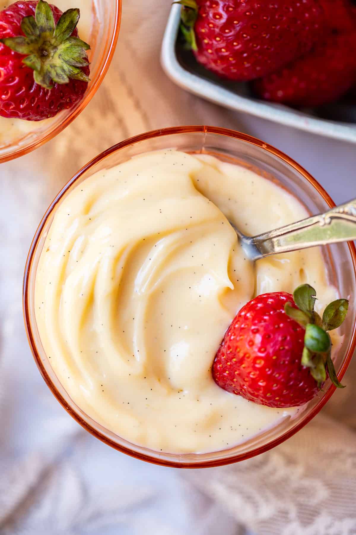 pink glass bowl filled with pudding made from scratch with a spoon and strawberry.