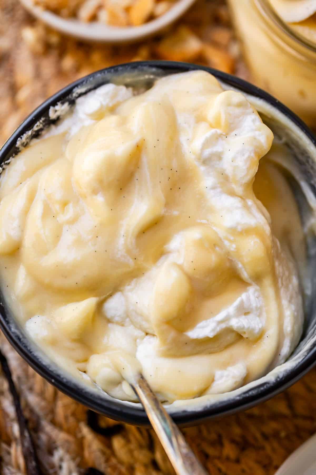 black bowl with homemade vanilla pudding and whipped cream swirled together by a spoon.