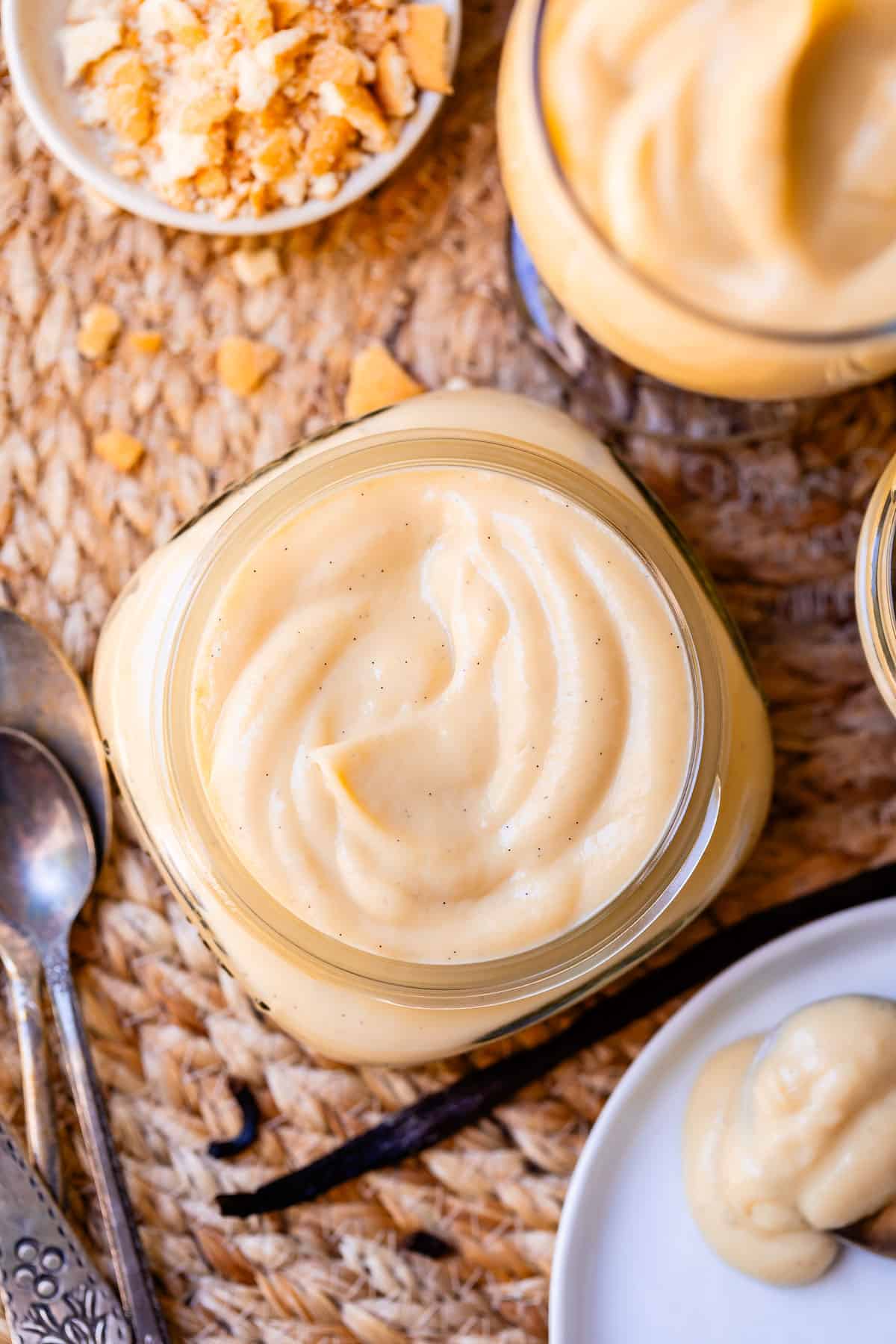 square jar filled with vanilla pudding from scratch on a mat with a spoon next to it.