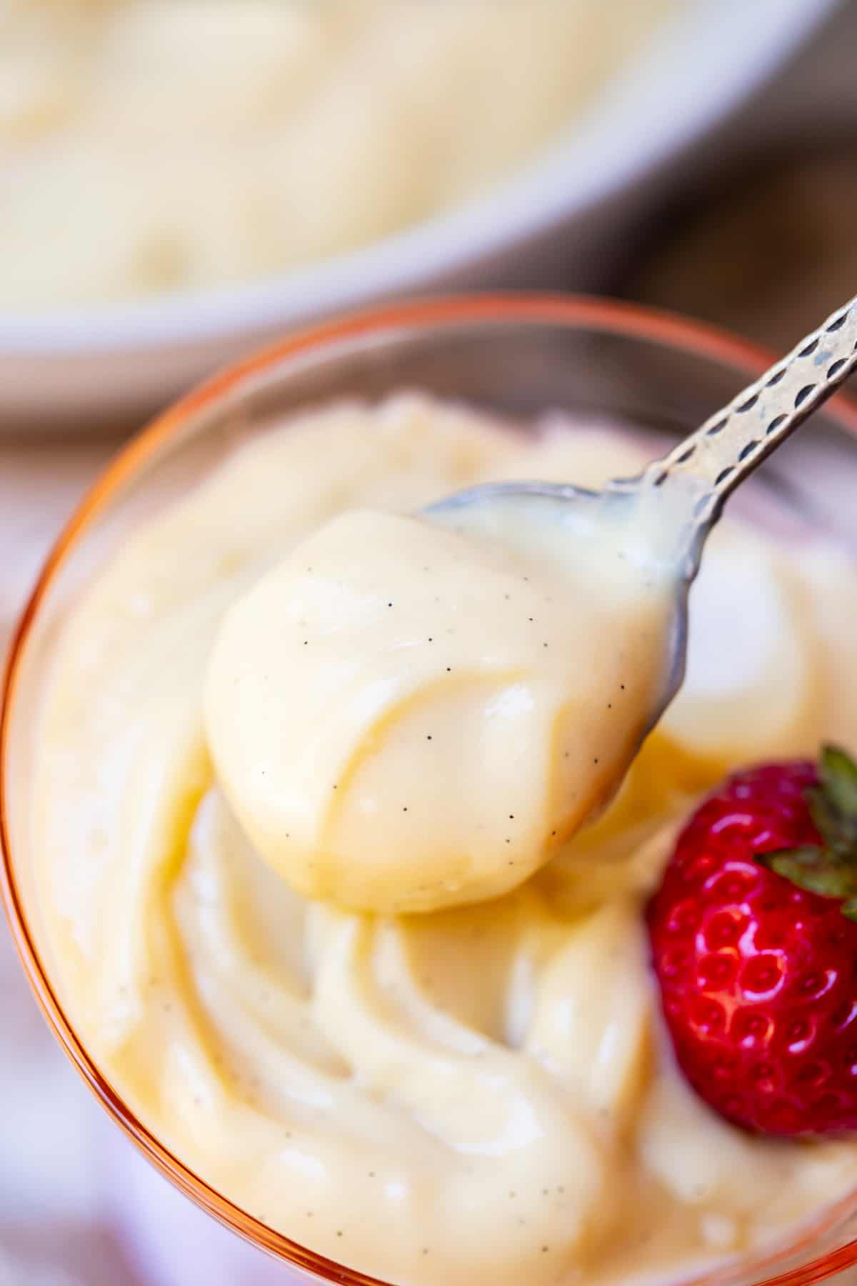 a spoon filled with vanilla pudding from scratch being lifted from a glass dish.