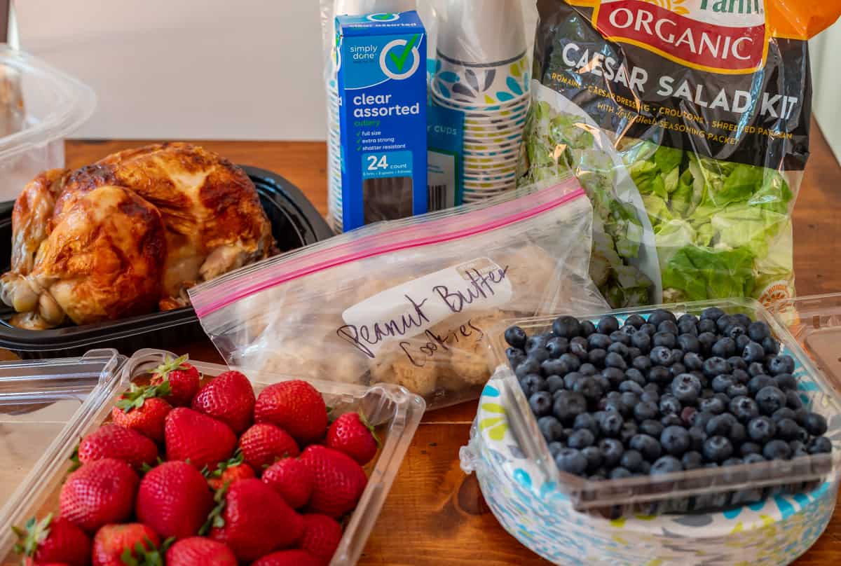 rotisserie chicken, strawberries, blueberries, salad kit, and cookie dough balls on a table.