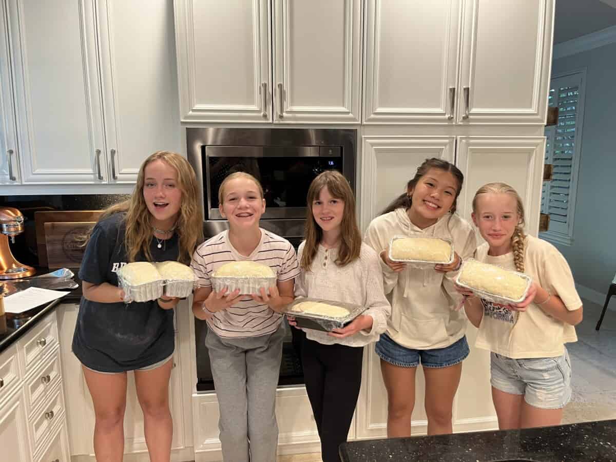 5 girls in a kitchen holding pans of rising bread.