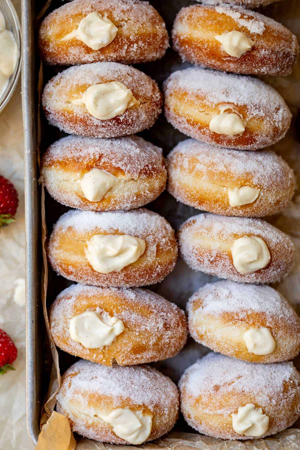 large metal tray filled with sideways stacked donuts that have been filled with cream.