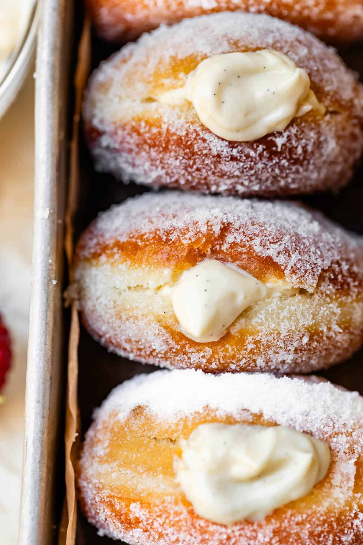 three sugar rolled donuts puffy with Bavarian cream filling in a metal baking dish.