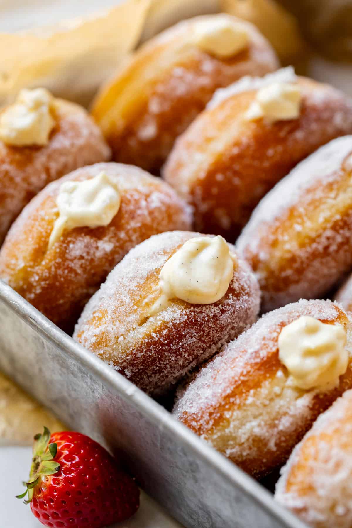 Homemade Bavarian Cream Donuts in a metal baking tray with a strawberry on the counter next to it.