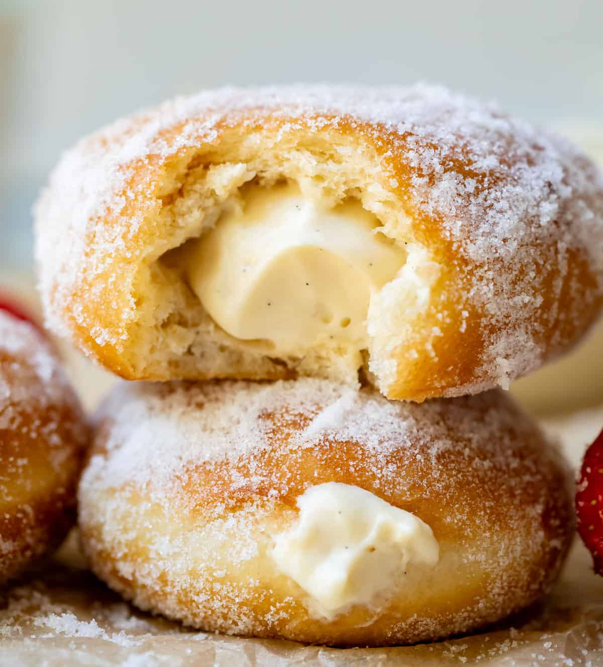 two stacked cream filled donuts and the top one has a bite taken from it, showing the cream filling.