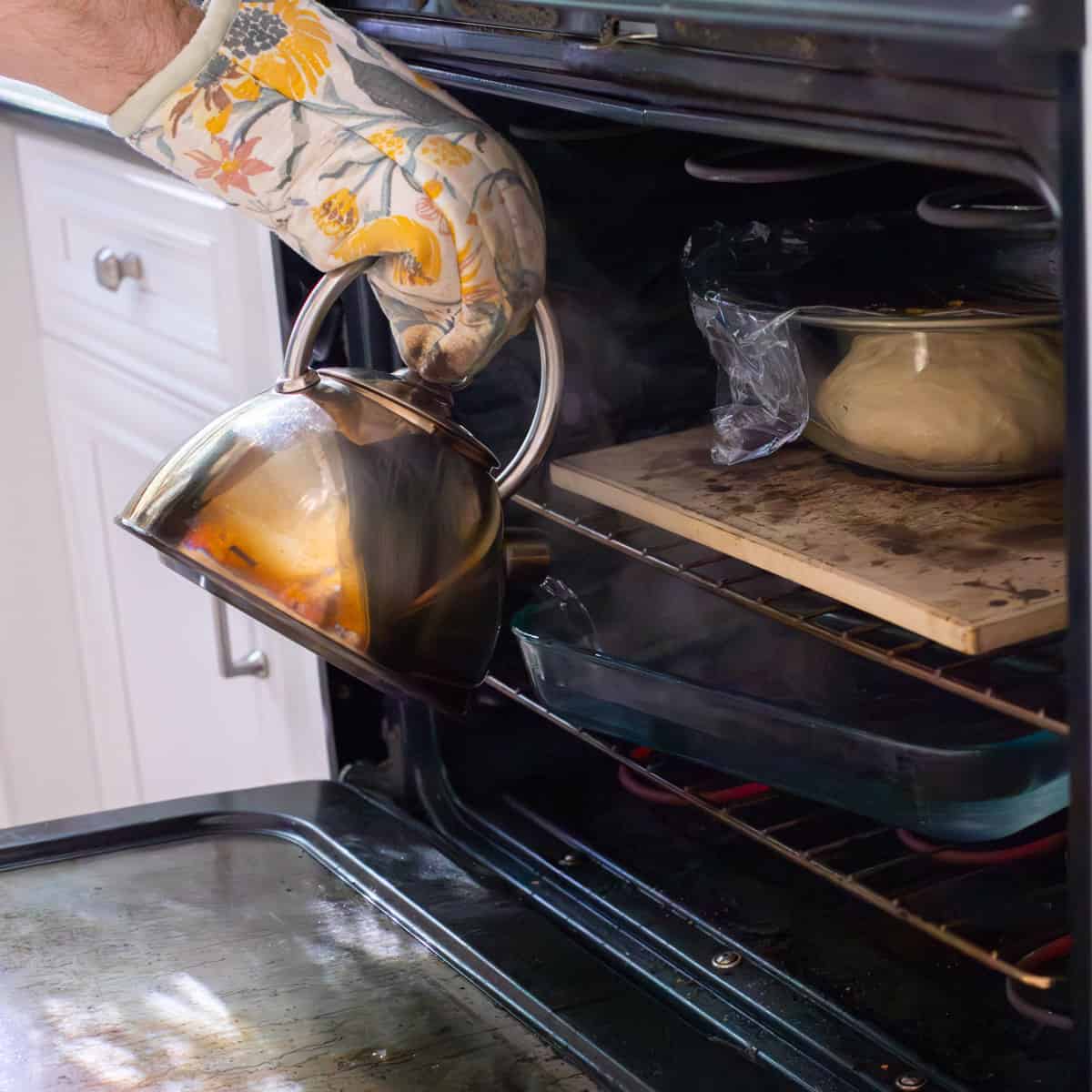 pouring hot water from a kettle into a pyrex dish under bowl of donut dough in oven.