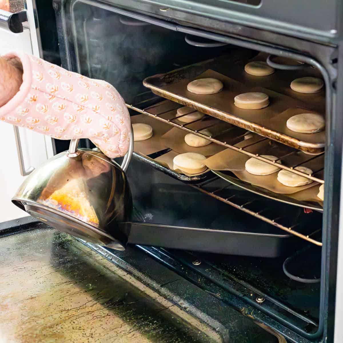 pouring water from a kettle into a pyrex dish under cut donuts ready for second rise in oven.