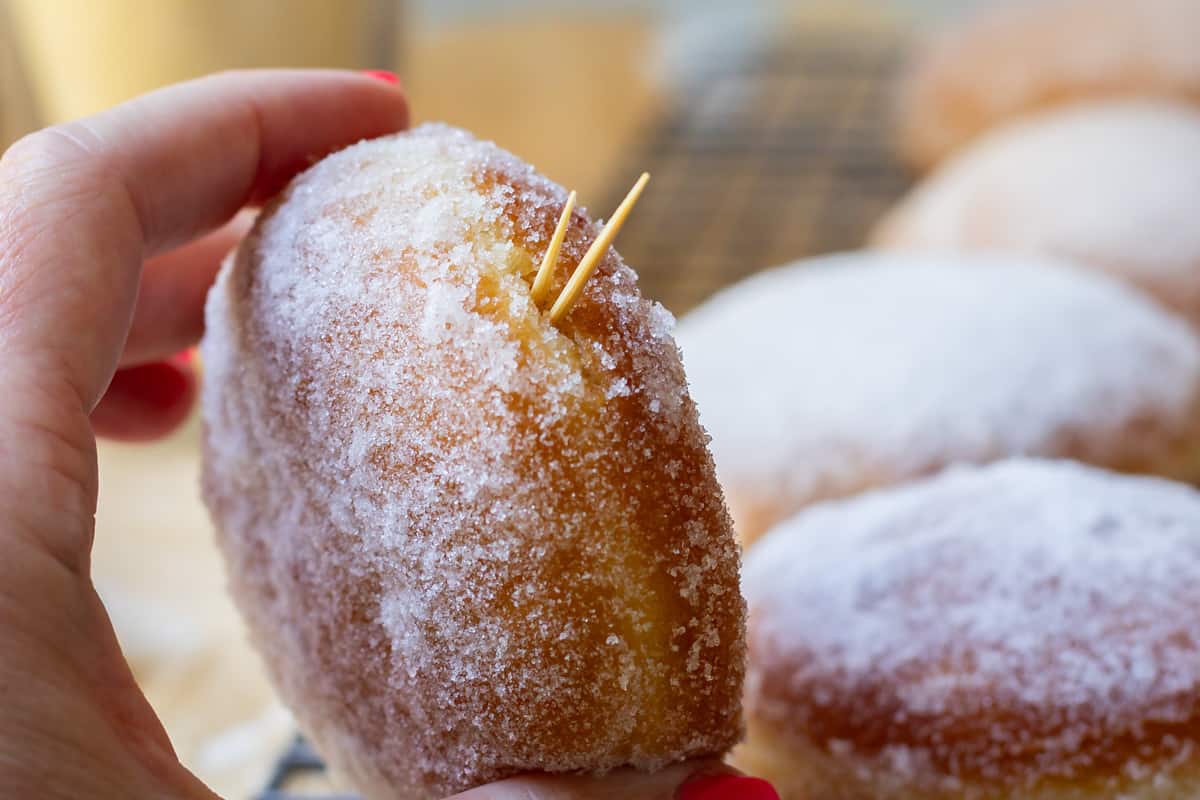 close up of coated donut with toothpicks in the hole to help with the filling process.