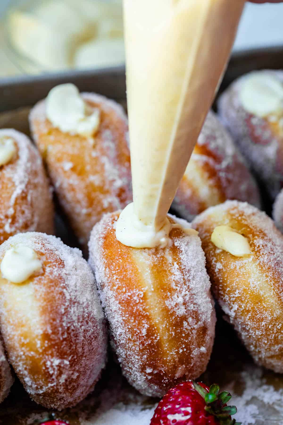 cream filled pastry bag filling a bavarian cream donut with several already filled donuts around it.