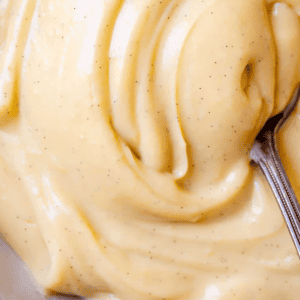 Close-up of creamy, yellow pastry cream with visible vanilla bean specks, smoothly swirled with a spoon. Text below reads, Pastry Cream, The Food Charlatan.