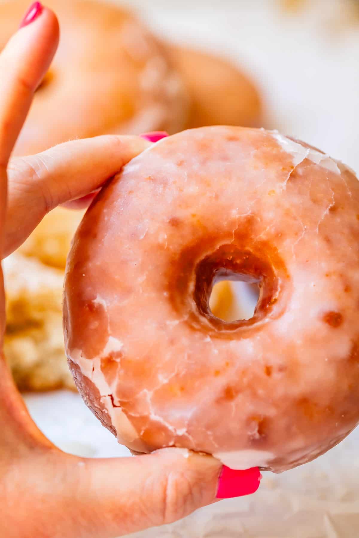 a hand holding up a perfectly glazed from scratch donut so you can see through the hole.