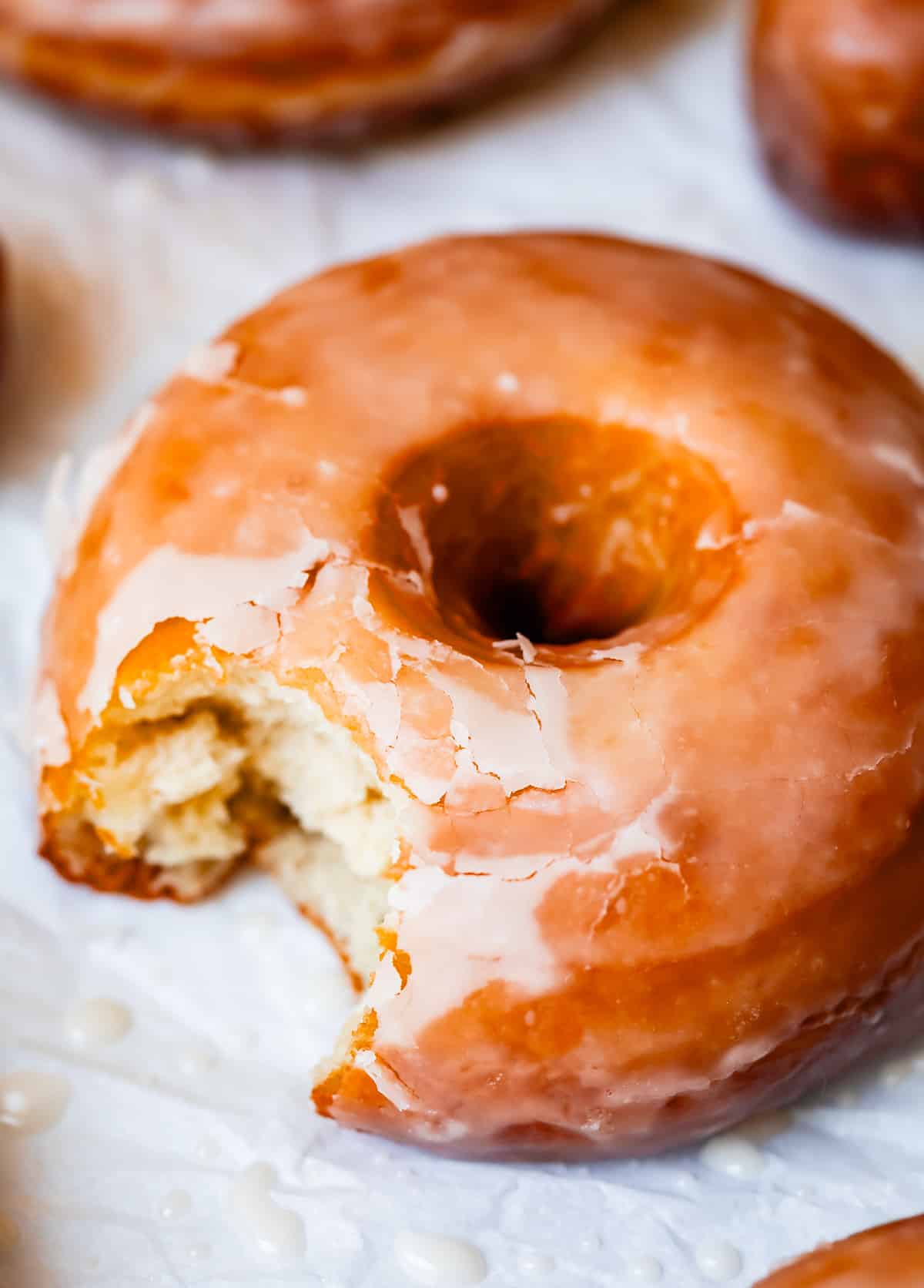 homemade glazed donut with a bite taken out of it on parchment paper.