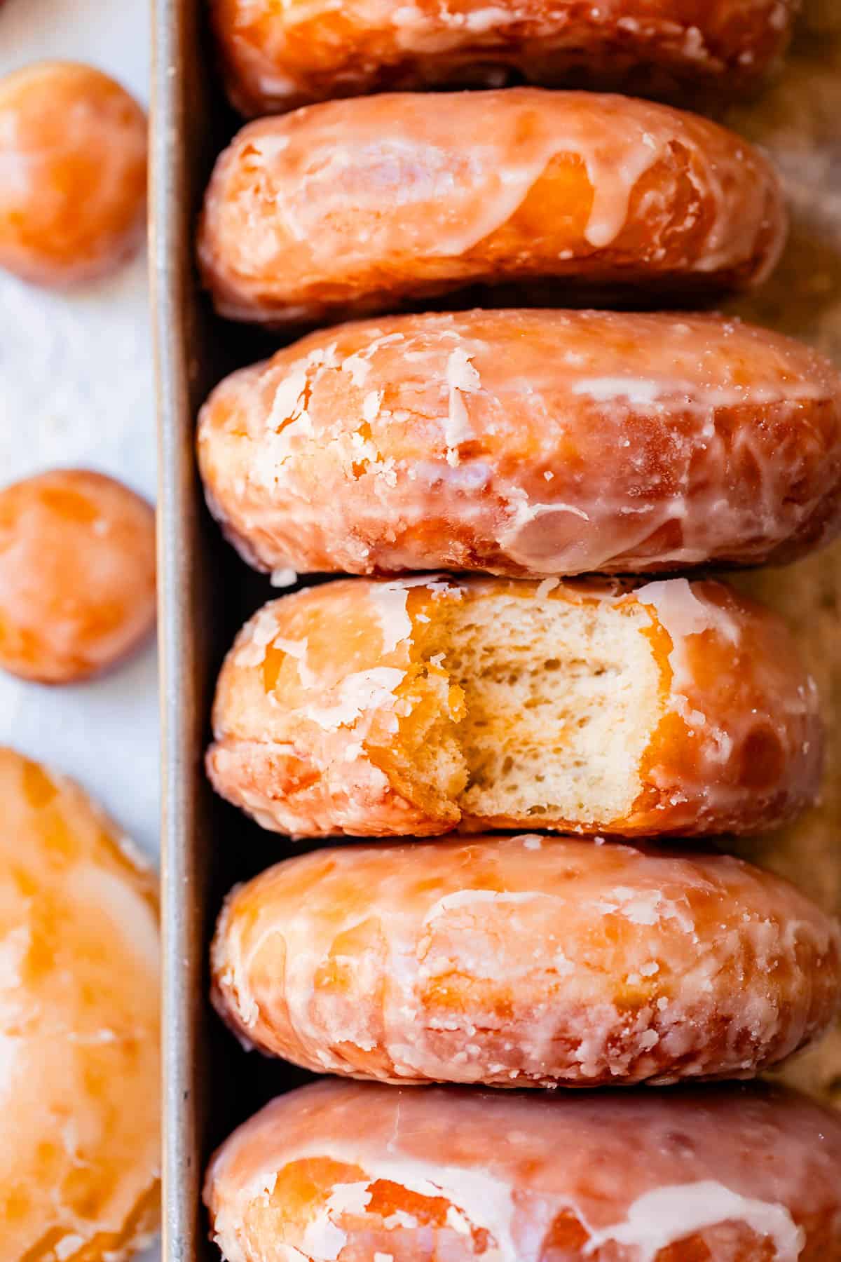 tray with 5 glazed donuts stacked sideways with a bite taken out of the middle donut.