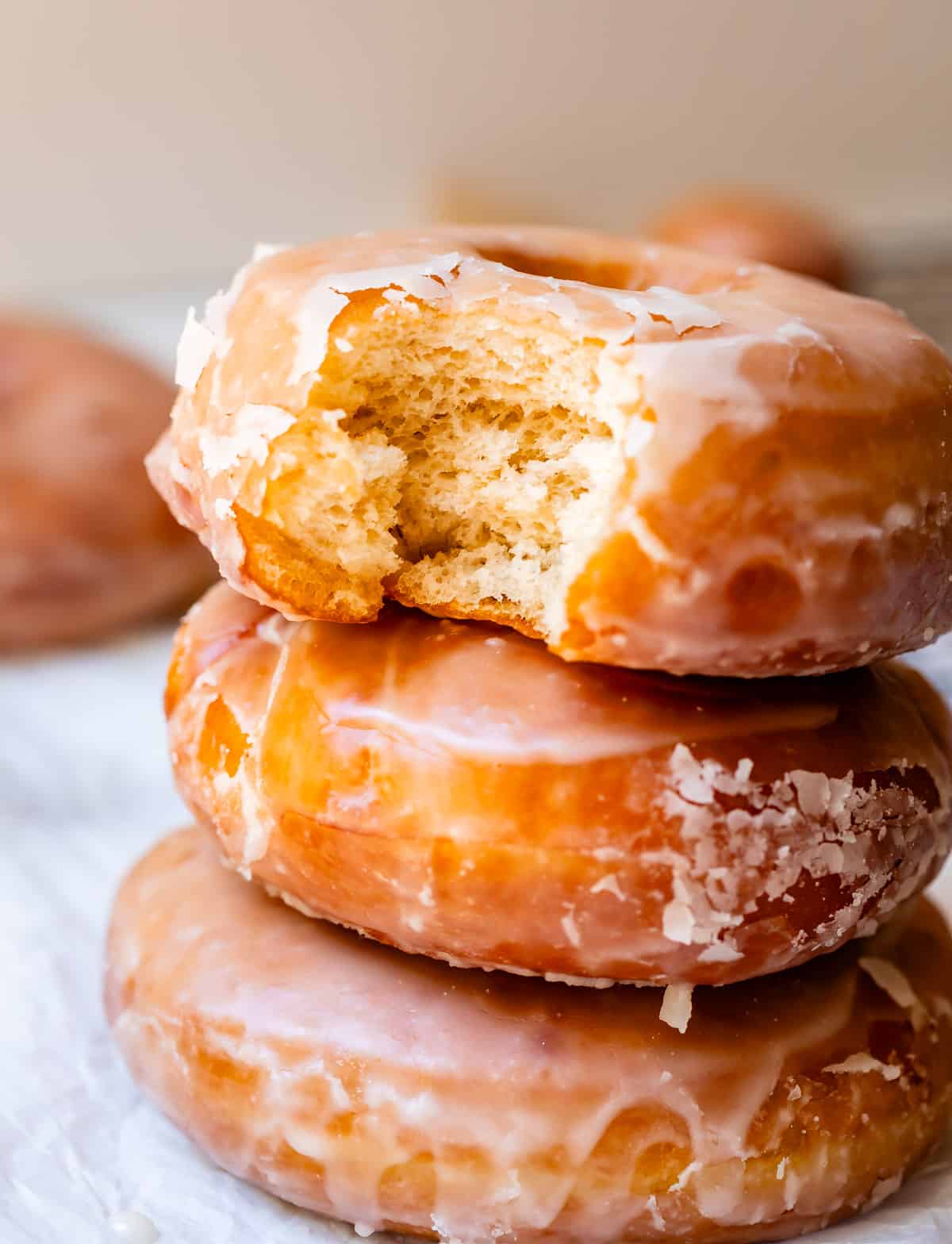 stack of three yeast donuts on parchment paper, with a bite taken out of the top donut.