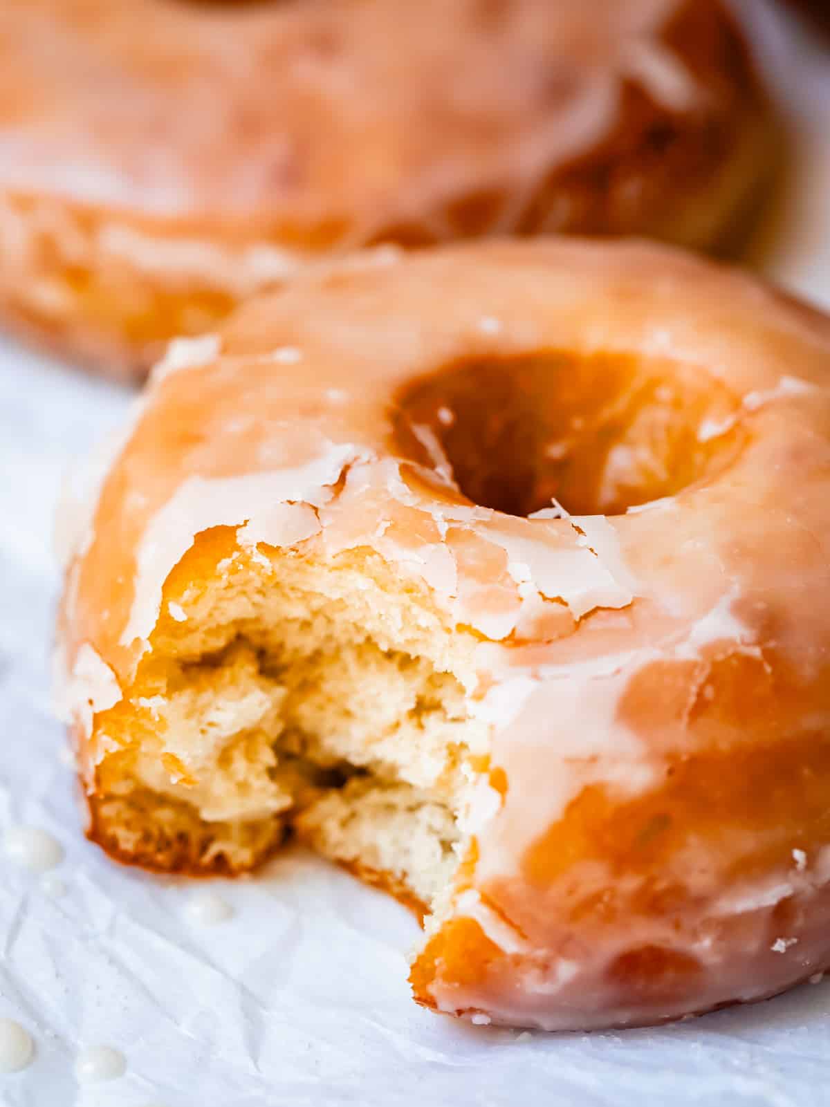 close up of one homemade donut with a bite taken out of it sitting on parchment paper.