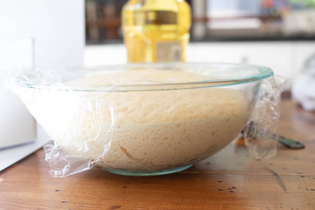 glass bowl with rising homemade donut dough rising, covered with plastic wrap.