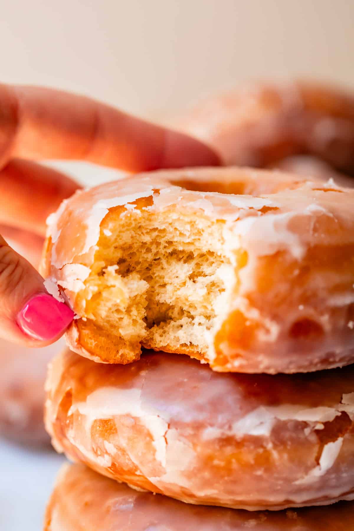 close up of hand reaching for a homemade glazed donut with a bite taken out of it.