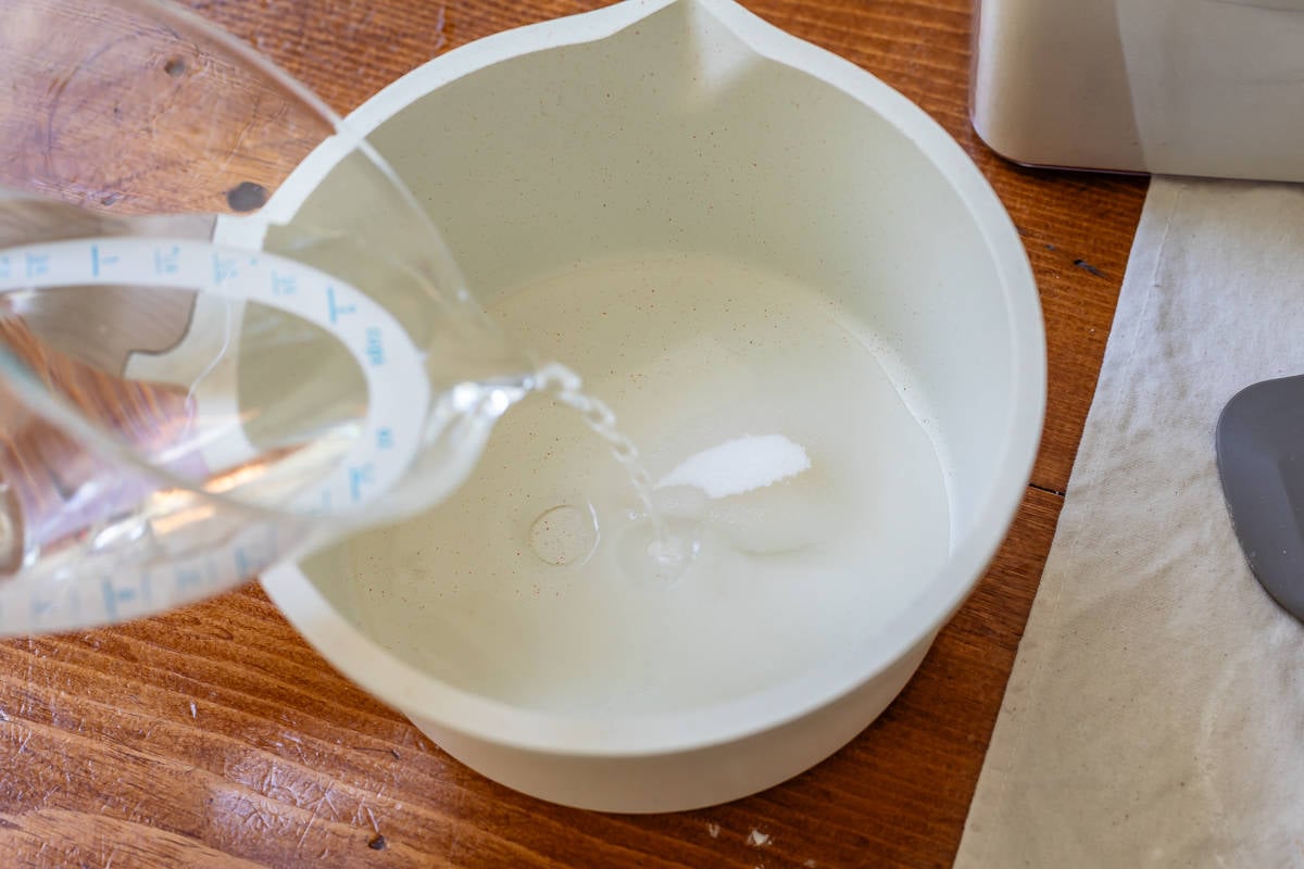 pouring water from a plastic liquid measuring cup into sugar in a mixing bowl for glaze.