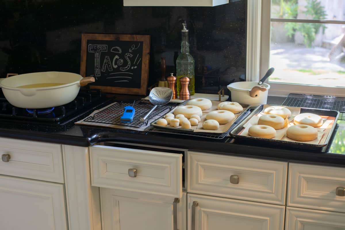 fry station set up - heated oil, drip tray, risen donuts and donut hole on parchment paper ready to fry.